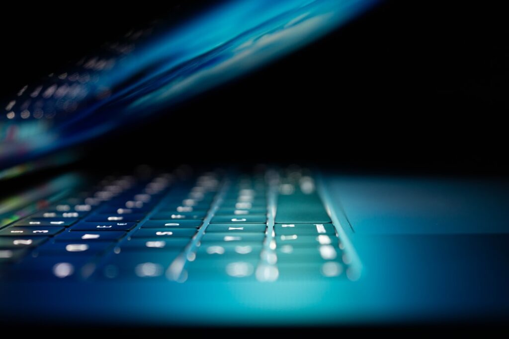 A person at a home office desk using a laptop with technical support on a monitor.