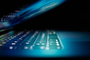 A person at a home office desk using a laptop with technical support on a monitor.